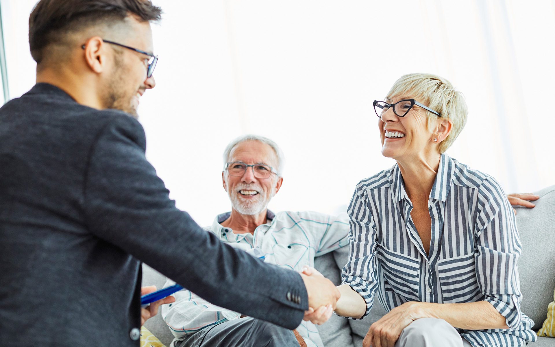 Your Claims Resource Center - Professional Shaking Hands with an Older Woman As She Sits on Her Living Room Couch with Her Partner